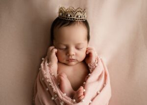 PHotos of newborn with princess crown in pink blanket.